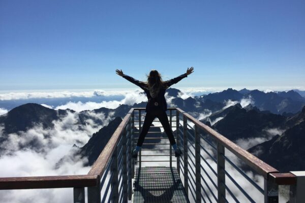 A woman stands on a viewing platform in Vysoké Tatry, Slovakia, surrounded by clouds and mountains, embracing freedom.